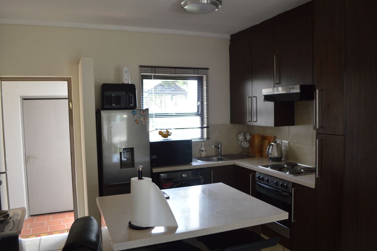Functional kitchen featuring dark wood cabinetry, stone countertops, a central island, and integrated appliances including an oven and hob.