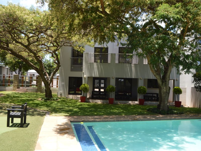Rear view of the apartment building featuring a well-maintained swimming pool, landscaped garden, and a private balcony with stainless steel balustrades.