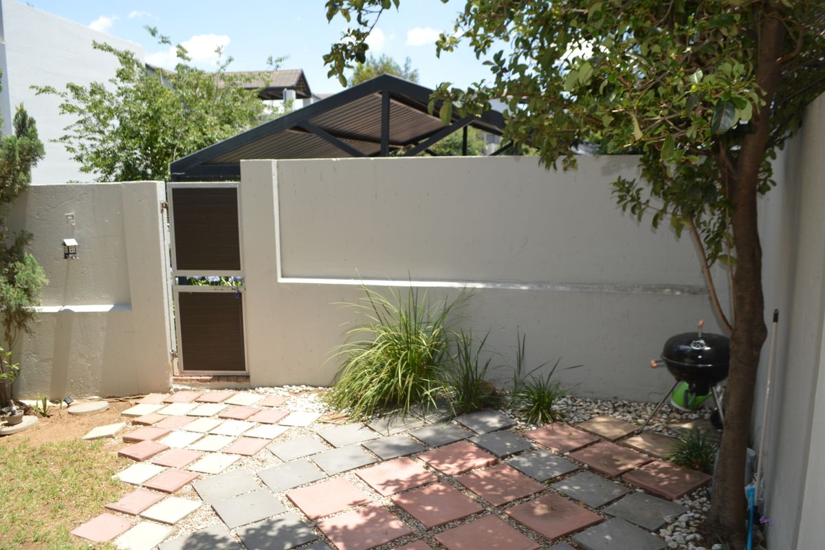 A private rear courtyard featuring a paved patio area, boundary wall, and a secure pedestrian gate with an adjacent carport structure.