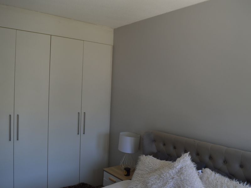 A bedroom featuring neutral-toned walls and functional built-in cupboards with modern handles, providing ample storage space.
