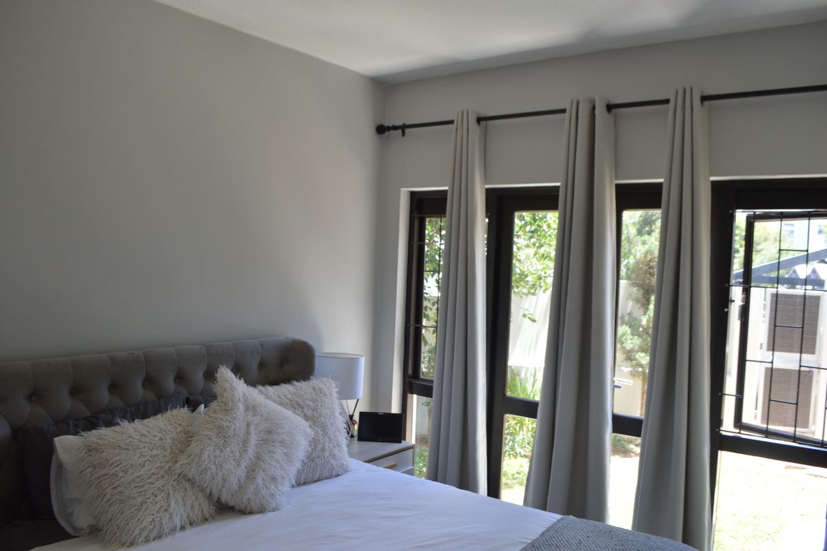A well-lit bedroom featuring large windows with security bars and neutral wall finishes, providing a bright and comfortable living space.