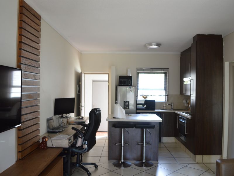 Open-plan living area featuring a functional kitchen with dark cabinetry, a central island, and tiled flooring, seamlessly integrated with a workspace area.