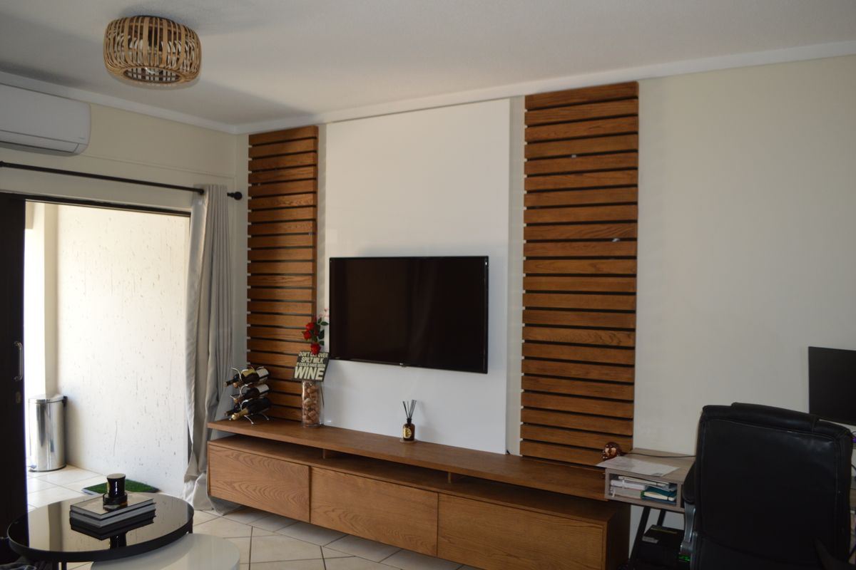 A modern living room featuring a custom timber slat media wall, built-in cabinetry, tiled flooring, and direct access to an outdoor patio area.