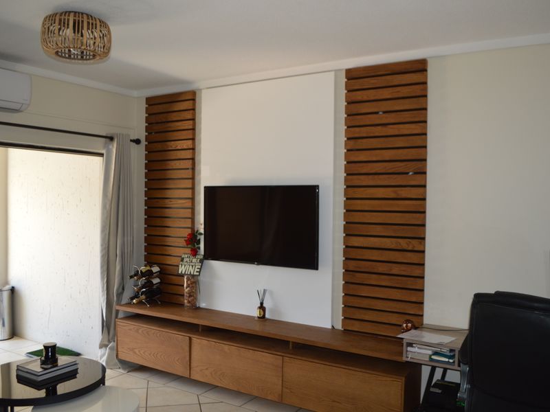 A modern living room featuring a custom timber slat media wall, built-in cabinetry, tiled flooring, and direct access to an outdoor patio area.