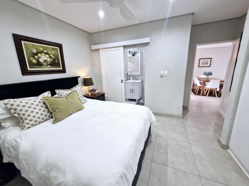 A well-maintained bedroom featuring tiled flooring, a ceiling fan, and a convenient en-suite vanity area with a sliding door.