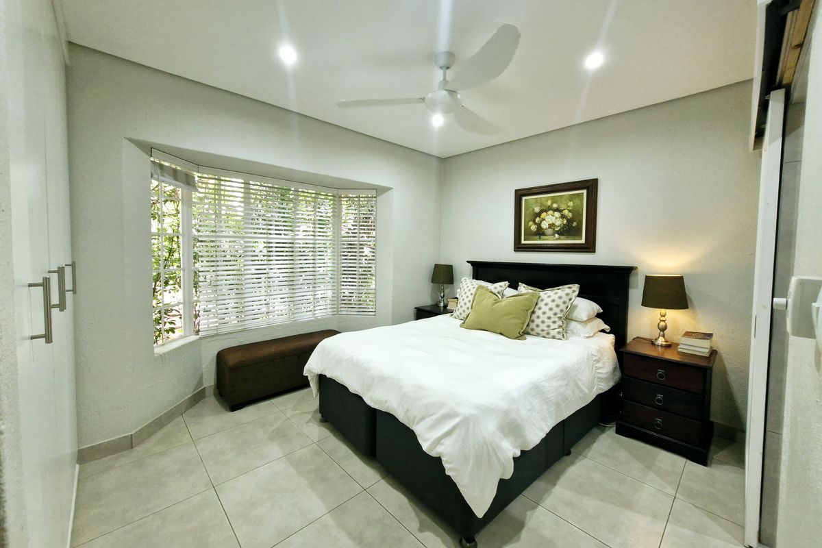A well-maintained bedroom featuring a large bay window, neutral tiled flooring, recessed lighting, a ceiling fan, and built-in wardrobe storage.