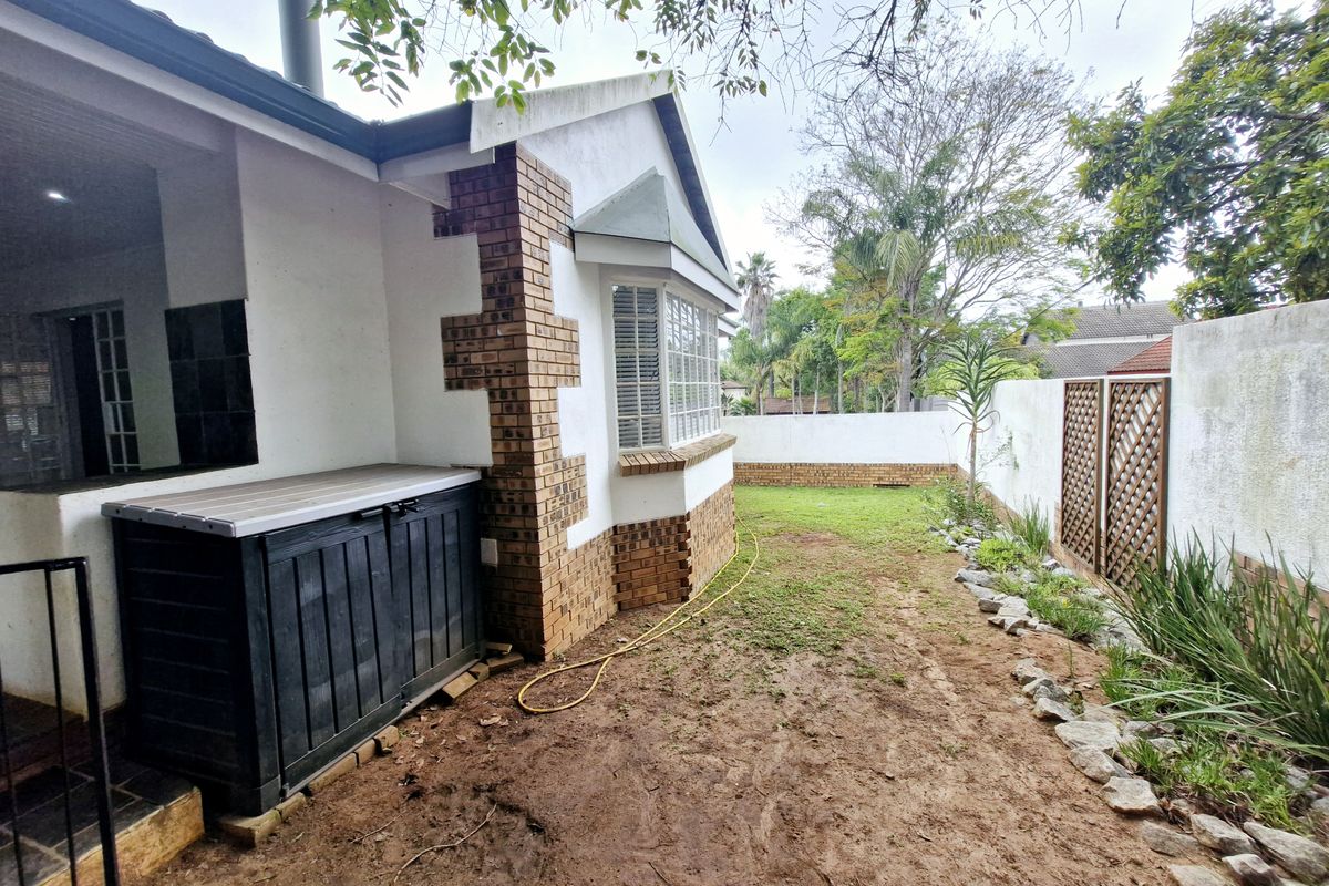 Rear exterior view of the townhouse featuring a brick-accented facade, bay window, and a private garden area with boundary walling.
