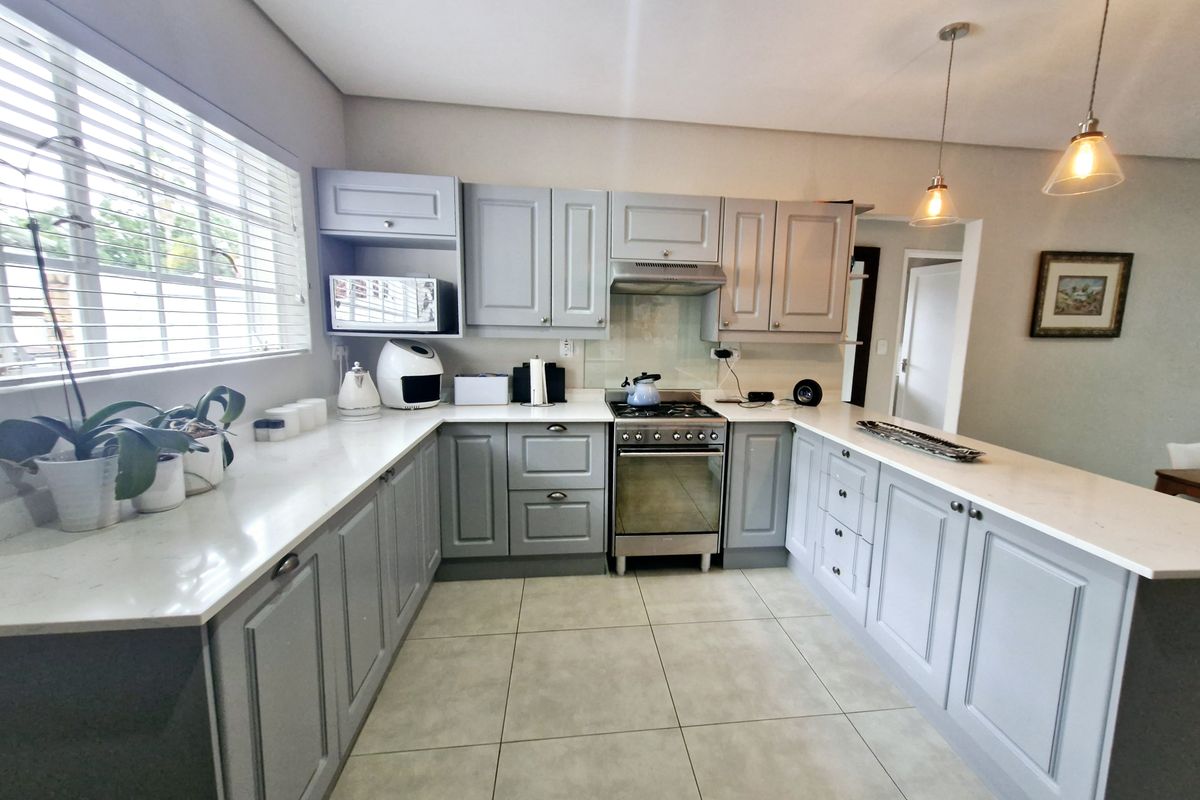 A well-maintained kitchen featuring light grey cabinetry, stone countertops, tiled flooring, and a freestanding gas stove with an extractor fan.