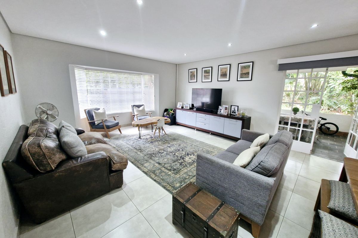 Spacious living room featuring neutral tiled flooring, recessed downlighting, and large windows that provide ample natural light, with direct access to an outdoor area.