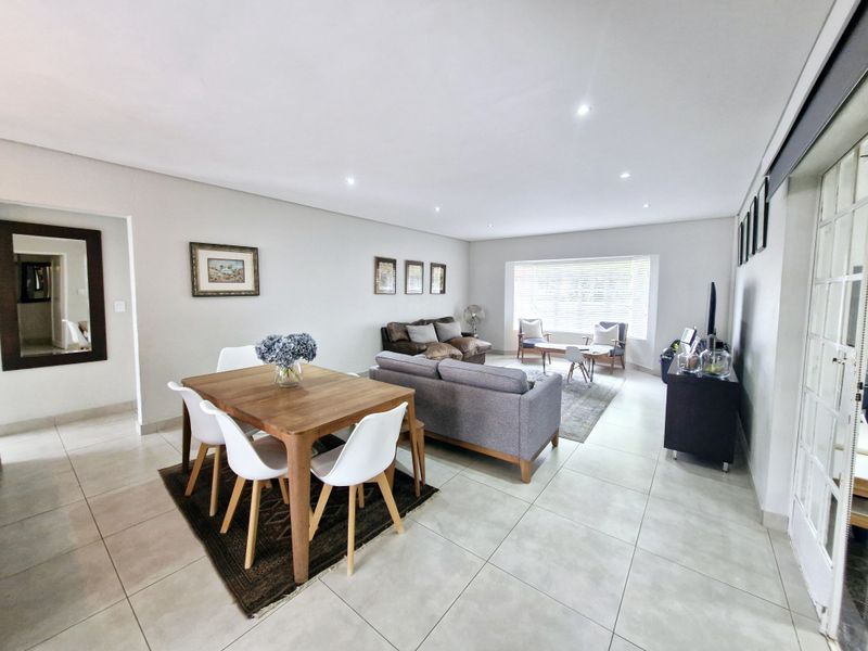 Spacious open-plan living and dining area featuring neutral tiled flooring, recessed downlighting, and large windows allowing for ample natural light.