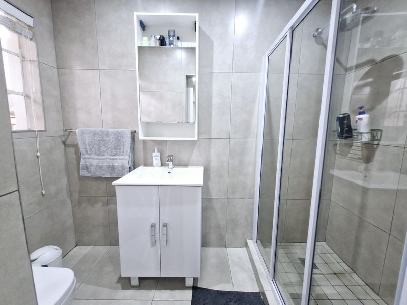 Modern bathroom featuring a vanity cabinet with basin, medicine cabinet, and a glass-enclosed shower with neutral floor-to-ceiling tiling.