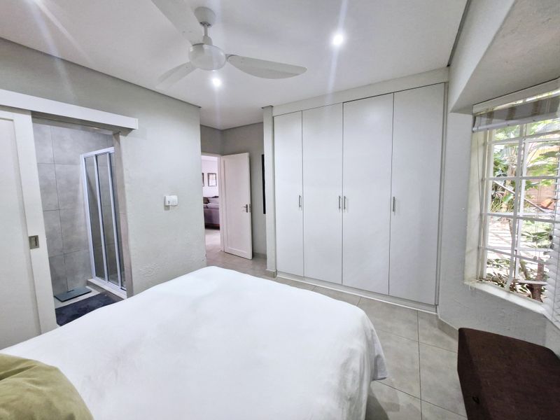 A well-maintained bedroom featuring built-in cupboards, tiled flooring, a ceiling fan, and direct access to an en-suite bathroom.