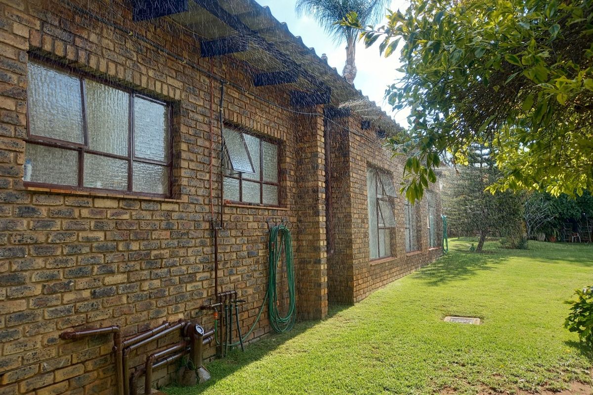 Rear view of the house featuring a classic face brick facade, steel-framed windows, and exposed timber rafters overlooking a well-maintained garden lawn.