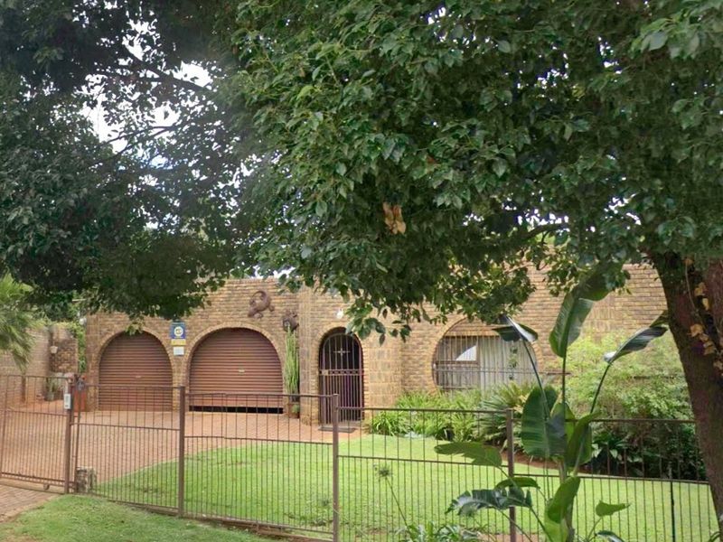 Front elevation of a brick house featuring a double garage with roller shutter doors, an arched entrance, and a paved driveway behind metal fencing.