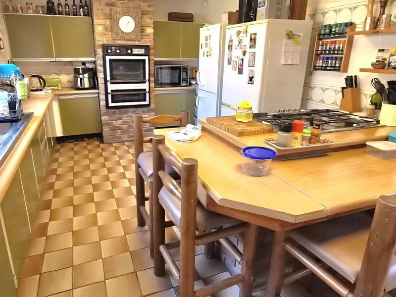 A dated kitchen featuring olive green cabinetry, a brick-encased built-in oven, gas hob, and tiled flooring, offering significant potential for a modern renovation.