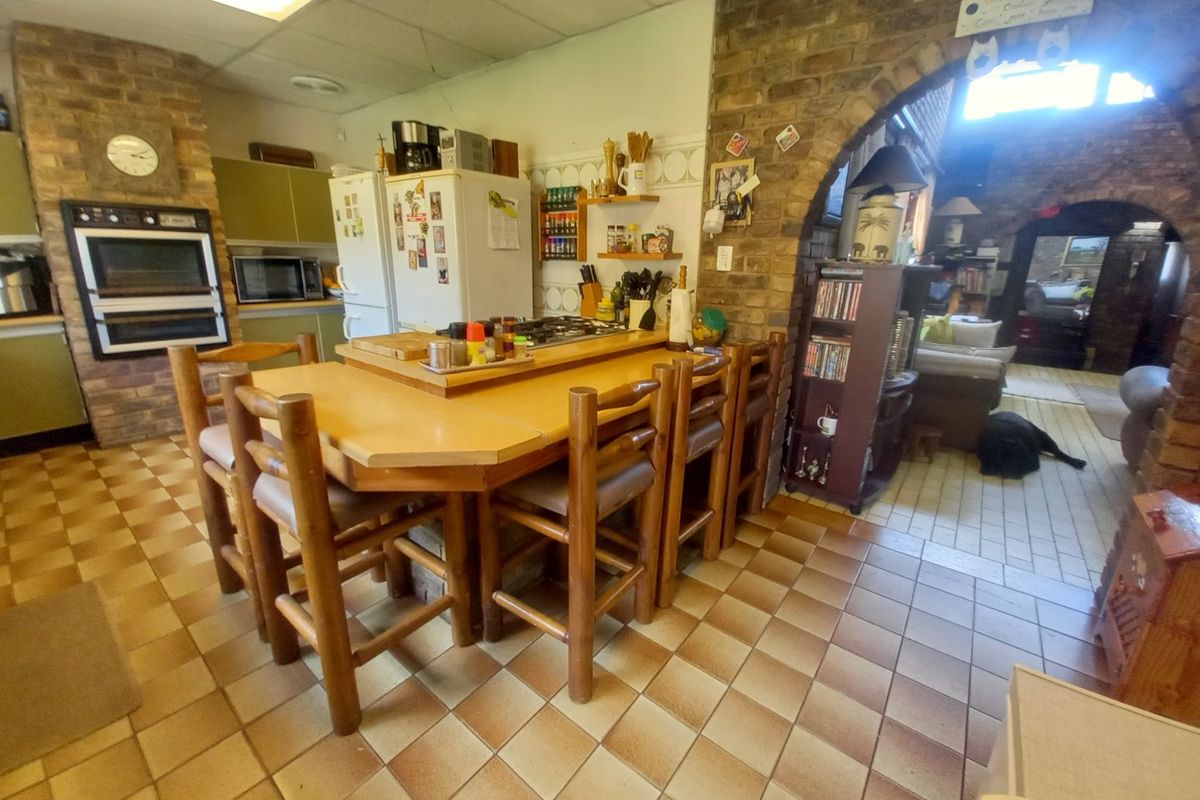 A dated kitchen featuring a brick accent wall, built-in oven, gas hob, and tiled flooring, with an open archway leading to the adjacent living area.