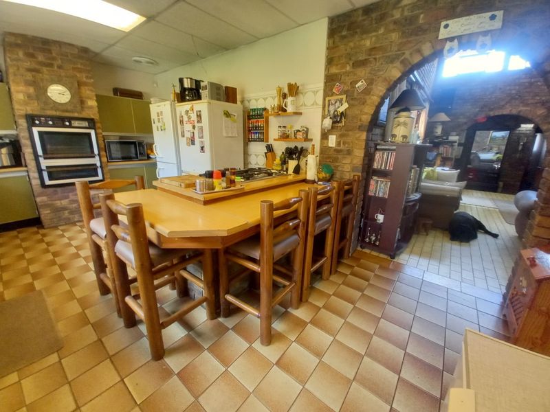 A dated kitchen featuring a brick accent wall, built-in oven, gas hob, and tiled flooring, with an open archway leading to the adjacent living area.