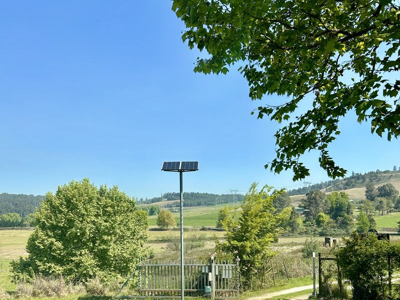 A scenic view of the property entrance featuring a gravel driveway, metal gate, and solar-powered lighting set against a rural landscape.