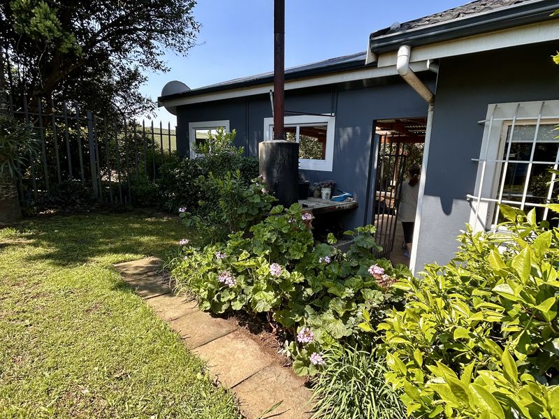 Rear exterior view of the property featuring a garden area, paved walkway, and an external fireplace with a chimney flue.