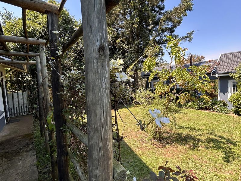A garden view featuring a rustic wooden pergola structure, a concrete walkway, and established lawn area adjacent to the main dwelling.