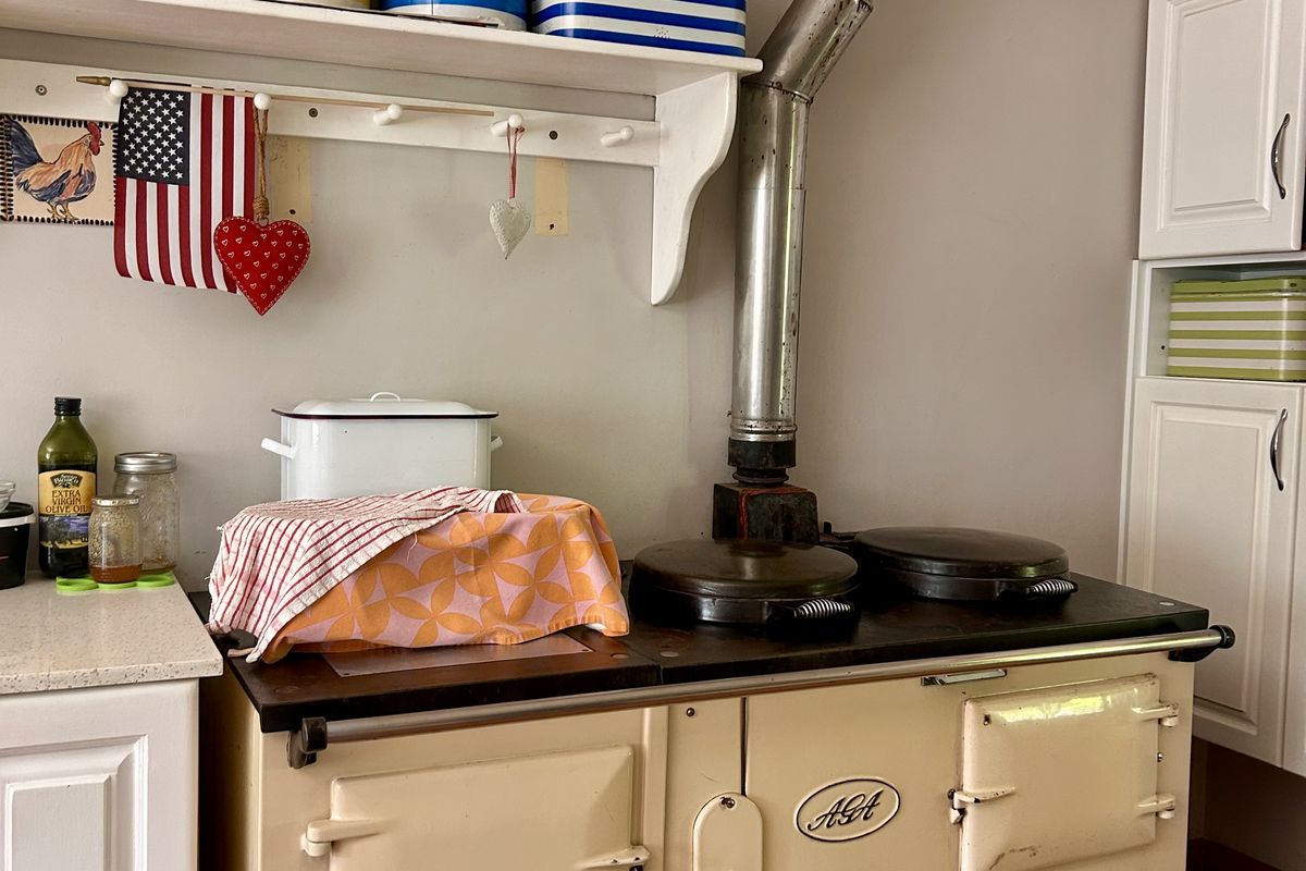 Kitchen area featuring a classic cream AGA range cooker with a metal flue, complemented by built-in cabinetry and traditional tiled flooring.