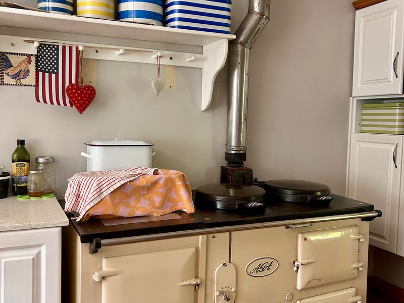 Kitchen area featuring a classic cream AGA range cooker with a metal flue, complemented by built-in cabinetry and traditional tiled flooring.