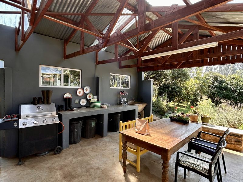 A spacious covered patio featuring exposed timber roof trusses, corrugated metal roofing, a built-in concrete prep area with sink, and polished concrete flooring.