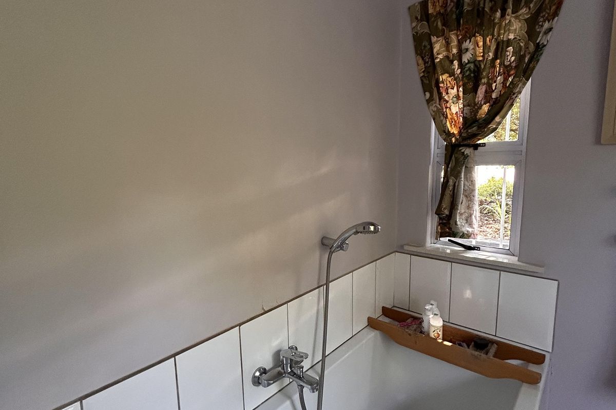 A functional bathroom featuring a built-in bathtub with a handheld shower mixer and a tiled splashback.