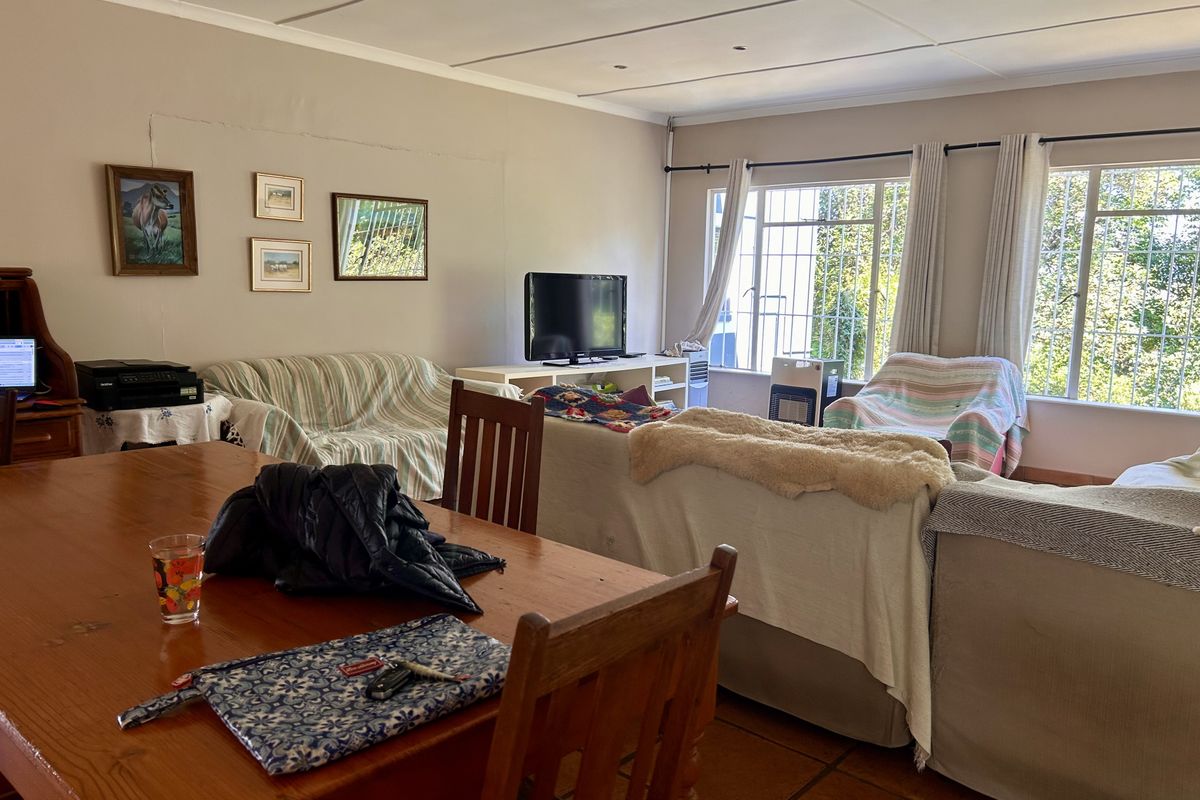 Spacious living area featuring tiled flooring and large windows with security bars, offering a functional layout with potential for cosmetic updates.