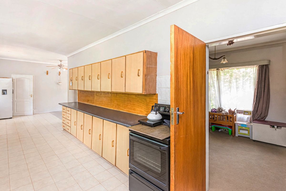 A functional kitchen featuring extensive built-in cabinetry, laminate countertops, and a freestanding oven, with tiled flooring and direct access to an adjacent living area.