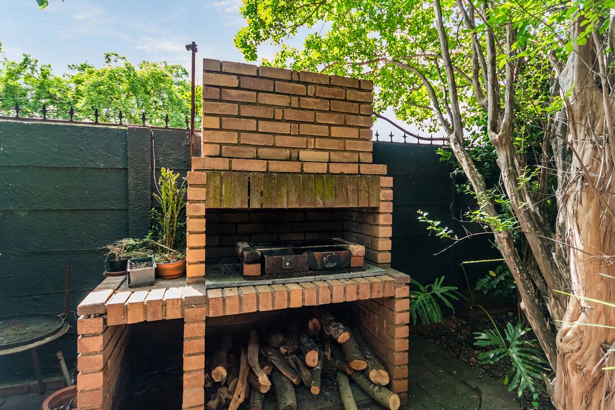 A traditional built-in brick braai area located in a private rear garden, featuring a masonry structure and paved base.