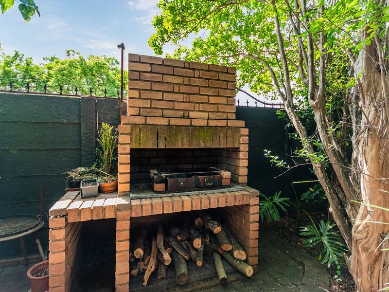 A traditional built-in brick braai area located in a private rear garden, featuring a masonry structure and paved base.