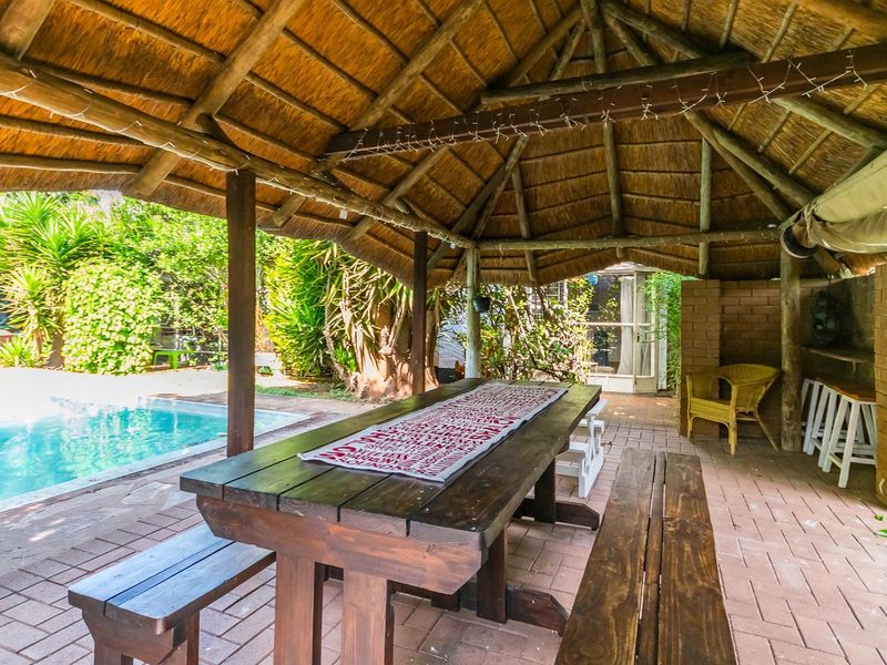 Covered outdoor patio featuring a traditional thatched roof, brick paving, and a built-in brick counter, overlooking a private swimming pool.