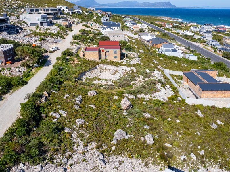 Aerial view of a vacant residential plot featuring natural coastal terrain and access to a gravel road in a developing neighborhood.