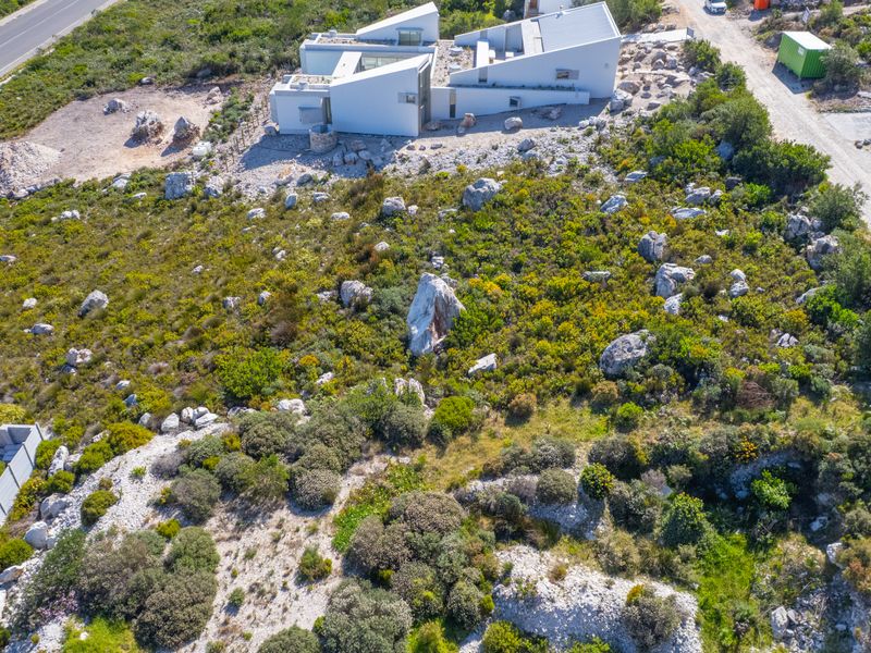 Aerial view of a modern residential property situated on a large, natural plot with rocky terrain and native vegetation.