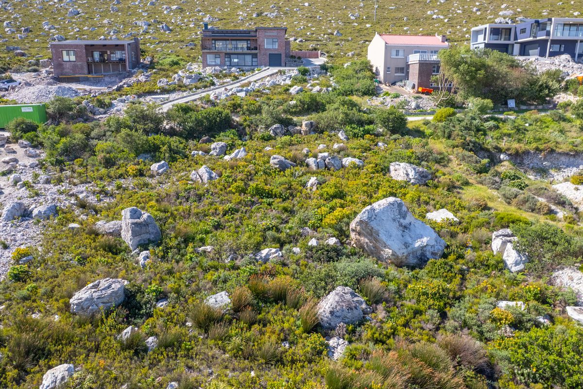An aerial view of a sloped, undeveloped residential plot featuring natural rock formations and indigenous fynbos vegetation in a mountainous coastal setting.