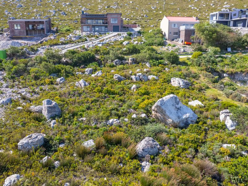 An aerial view of a sloped, undeveloped residential plot featuring natural rock formations and indigenous fynbos vegetation in a mountainous coastal setting.