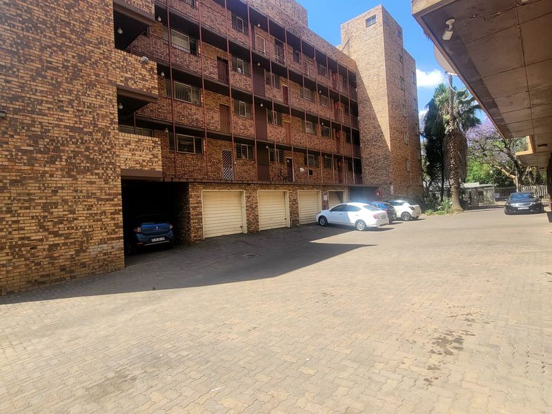 Exterior view of a multi-story face-brick apartment building featuring a paved driveway and integrated garage parking bays.