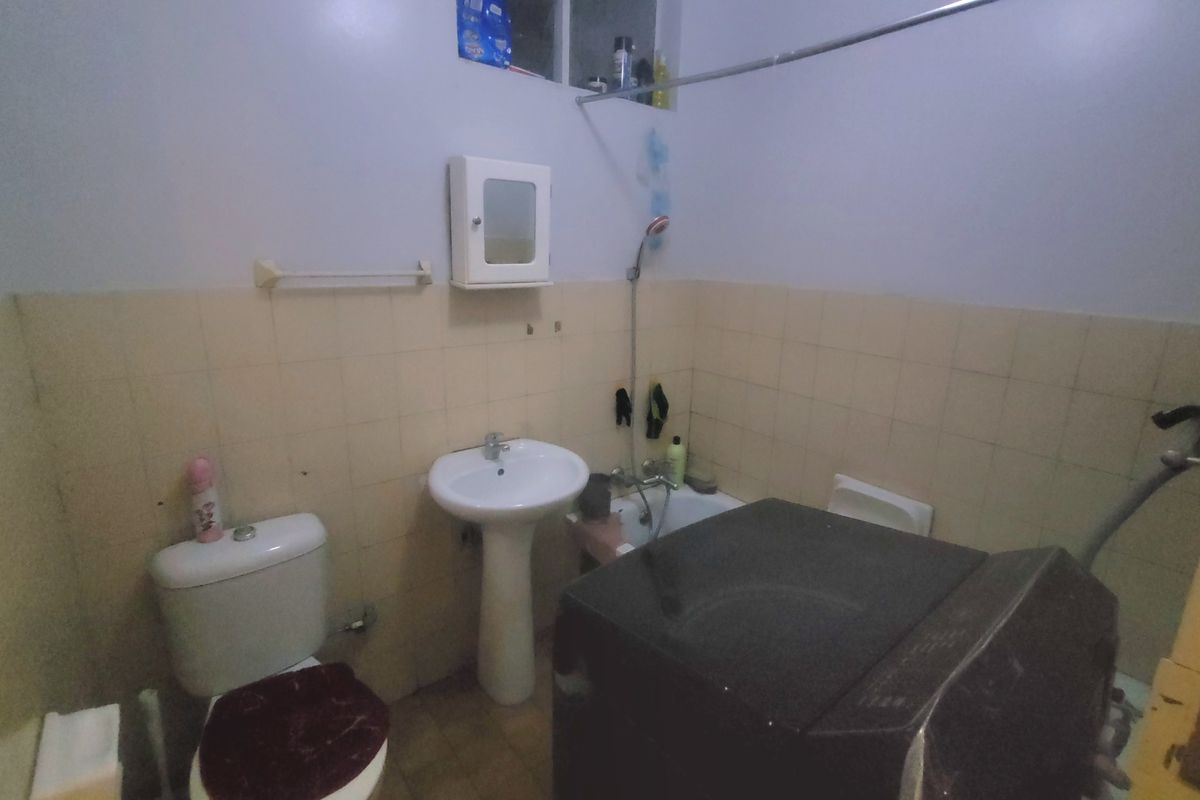A functional bathroom featuring a pedestal basin, toilet, and bathtub with tiled walls and flooring, currently showing signs of wear and dated finishes.