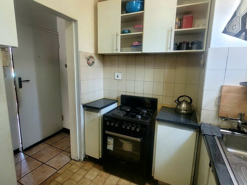 A compact kitchen featuring built-in cabinetry, a tiled backsplash, stainless steel sink, and a freestanding stove, with tiled flooring throughout.