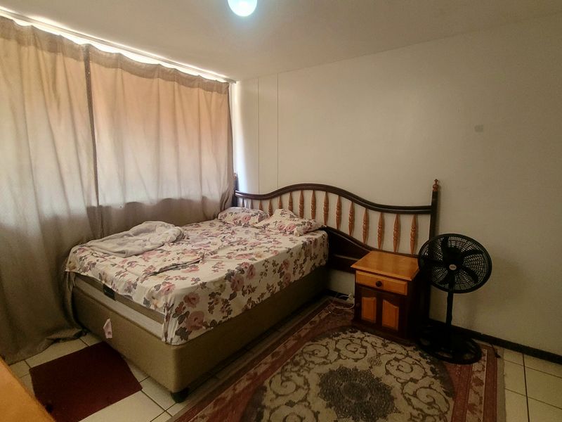 A functional bedroom featuring tiled flooring and a built-in cupboard, offering a neutral space ready for personalization.