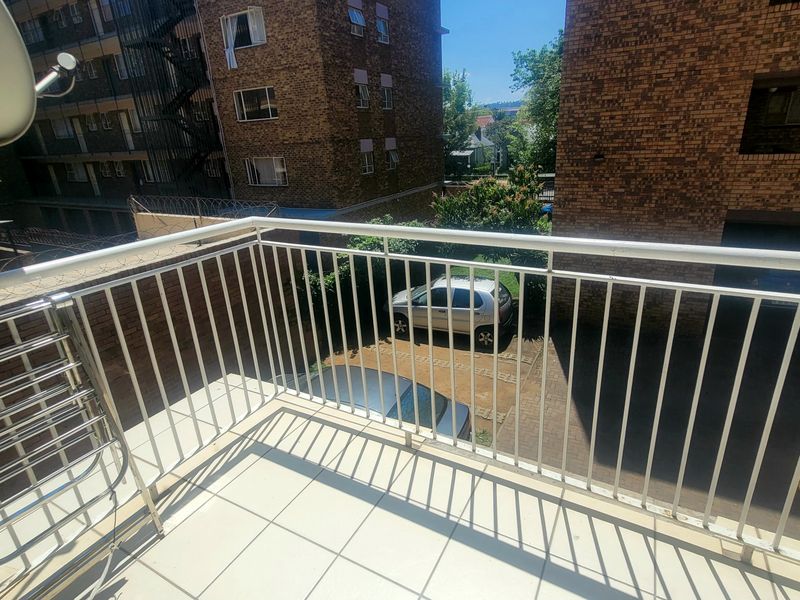 A functional balcony featuring a white metal balustrade and tiled flooring, overlooking the complex parking area.
