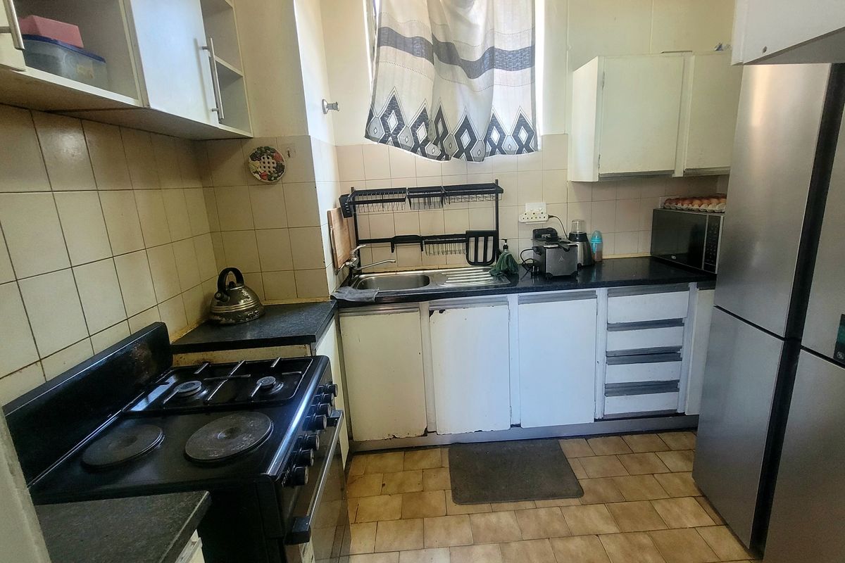 A compact kitchen featuring a gas stove, stainless steel sink, tiled backsplash, and built-in cabinetry with laminate countertops.