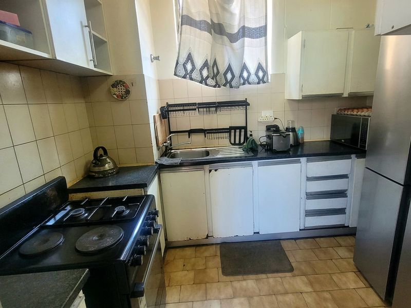 A compact kitchen featuring a gas stove, stainless steel sink, tiled backsplash, and built-in cabinetry with laminate countertops.