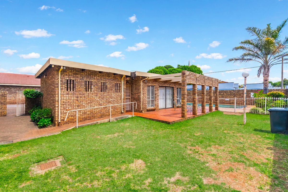 Rear view of the apartment featuring a brick facade, a covered patio area, and access to the garden and pool area.