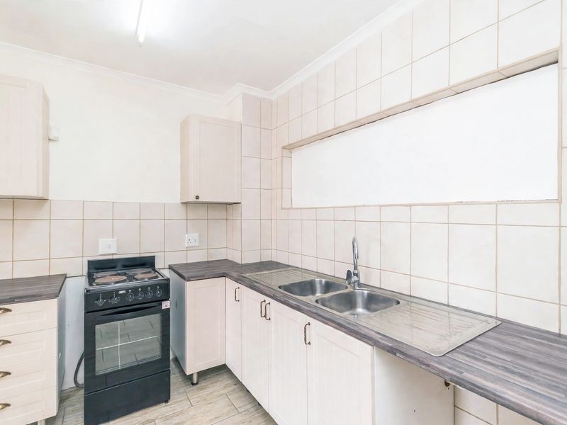 A functional kitchen featuring light-toned cabinetry, laminate countertops, a double stainless steel sink, and a freestanding stove with tiled splashbacks.