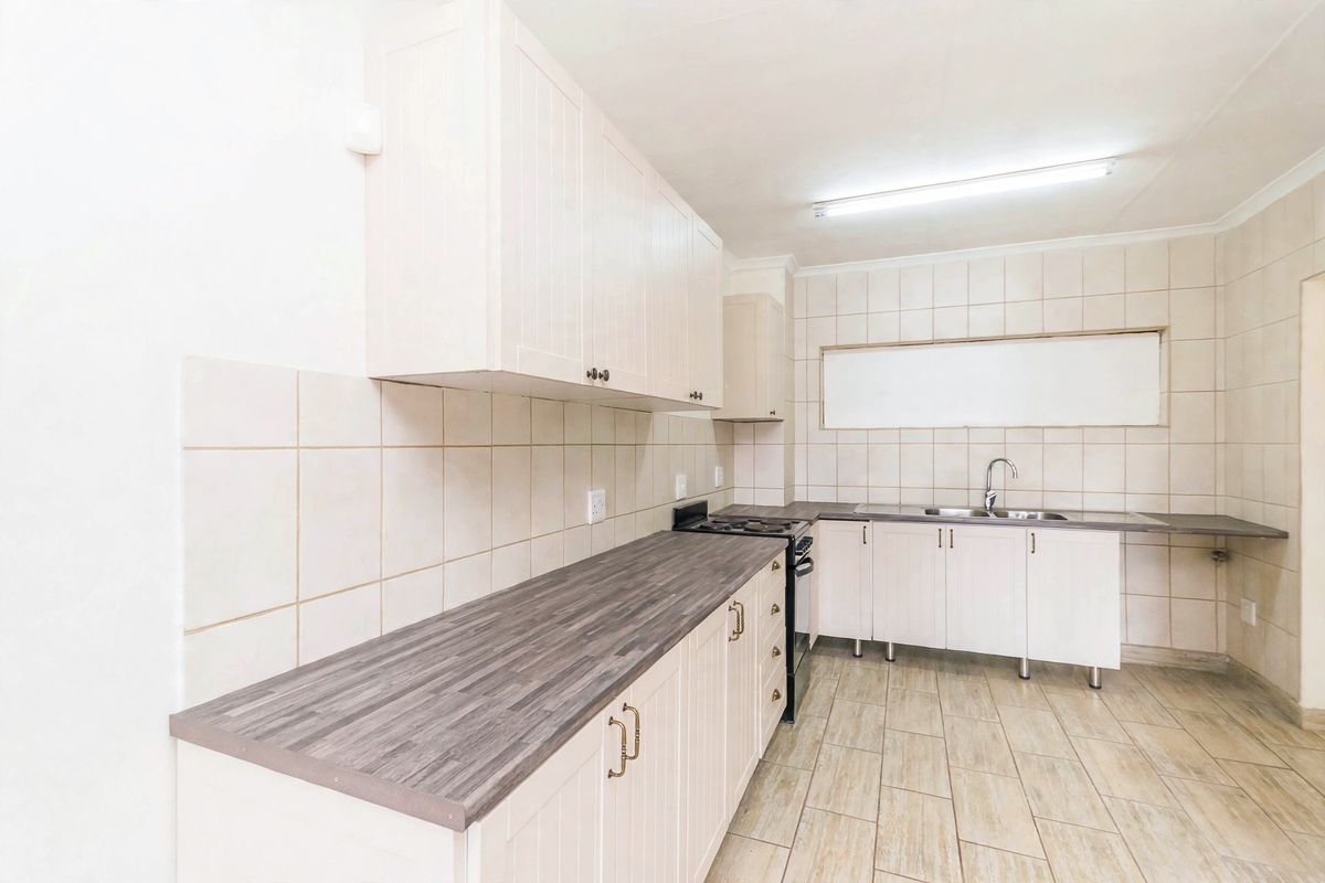 A functional kitchen featuring light-toned cabinetry, dark laminate countertops, a stainless steel sink, and tiled backsplash with neutral ceramic flooring.