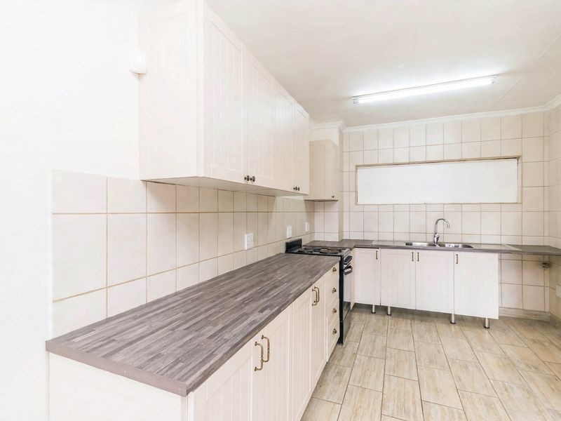 A functional kitchen featuring light-toned cabinetry, dark laminate countertops, a stainless steel sink, and tiled backsplash with neutral ceramic flooring.