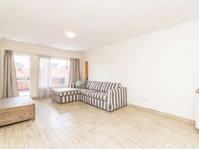 Bright and spacious living area featuring neutral tiled flooring, coved ceilings, and direct access to an outdoor balcony through a sliding glass door.