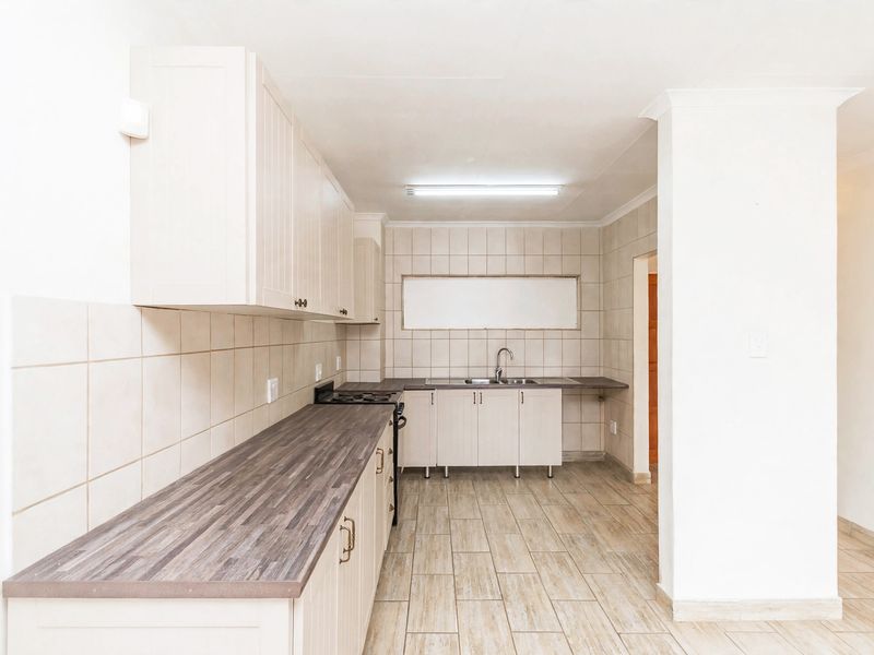 A clean, functional kitchen featuring light-toned cabinetry, dark laminate countertops, tiled backsplash, and durable ceramic floor tiles.